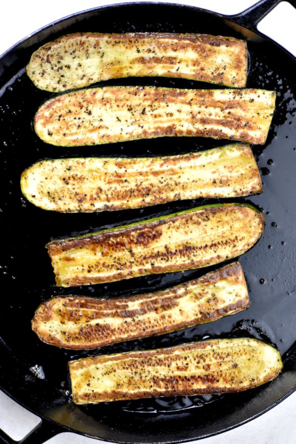 Cooked zucchini halves in a cast iron skillet.